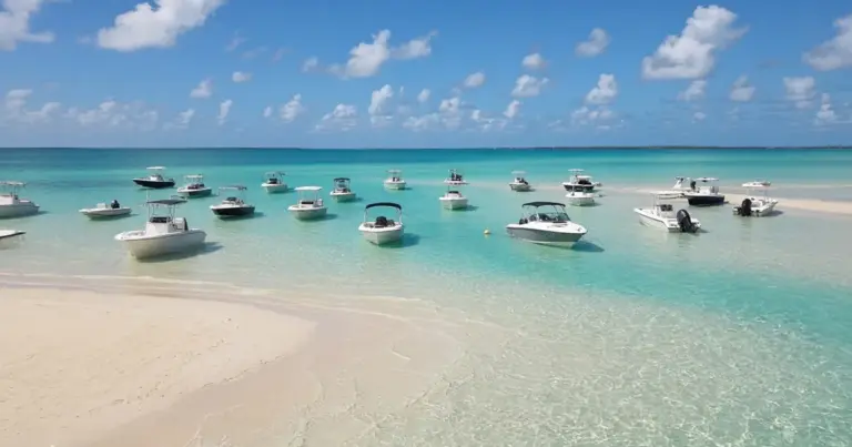 Boats anchored in clear turquoise water off a white sandbar on a summer day