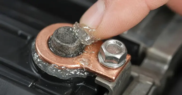 Finger applying clear grease to a copper ring terminal on a battery post